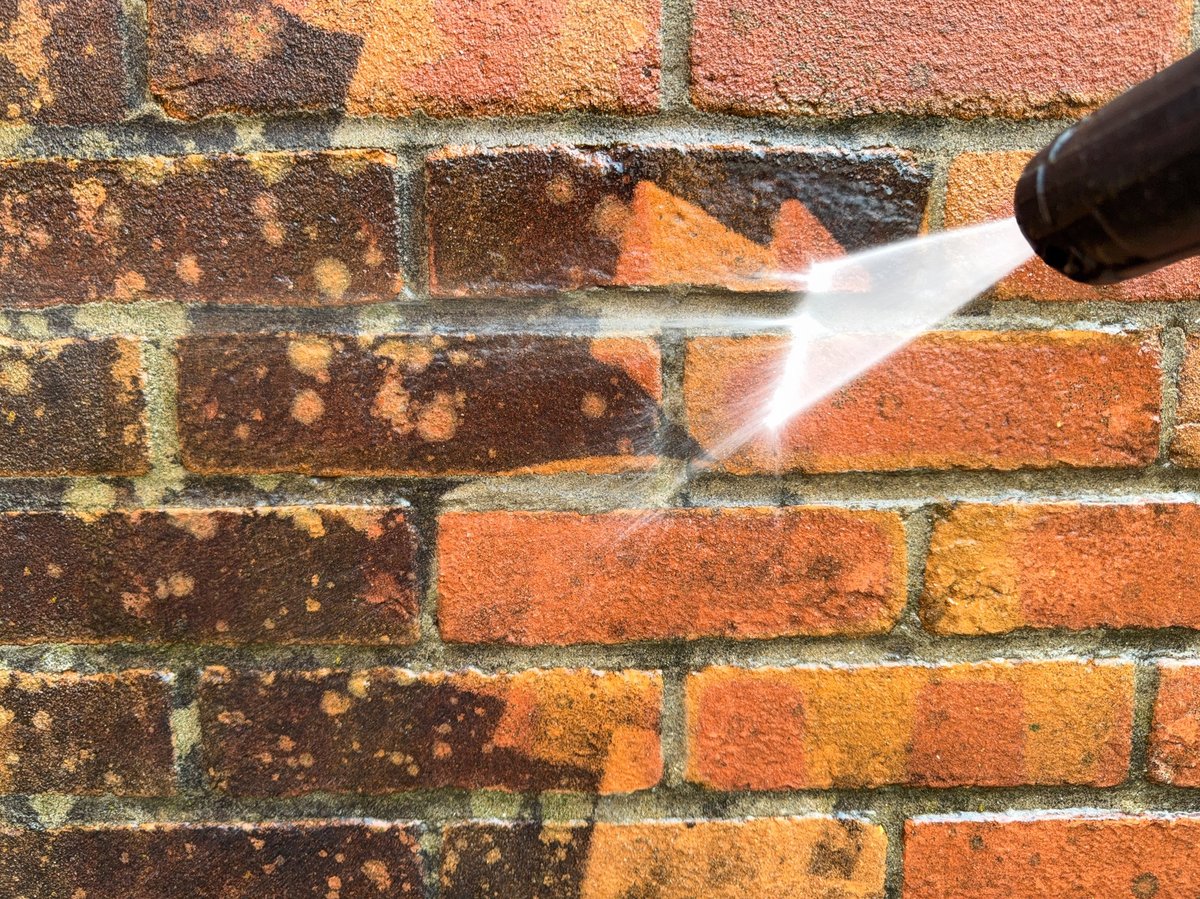 Pressure washer cleaning dirty bricks on an exterior wall